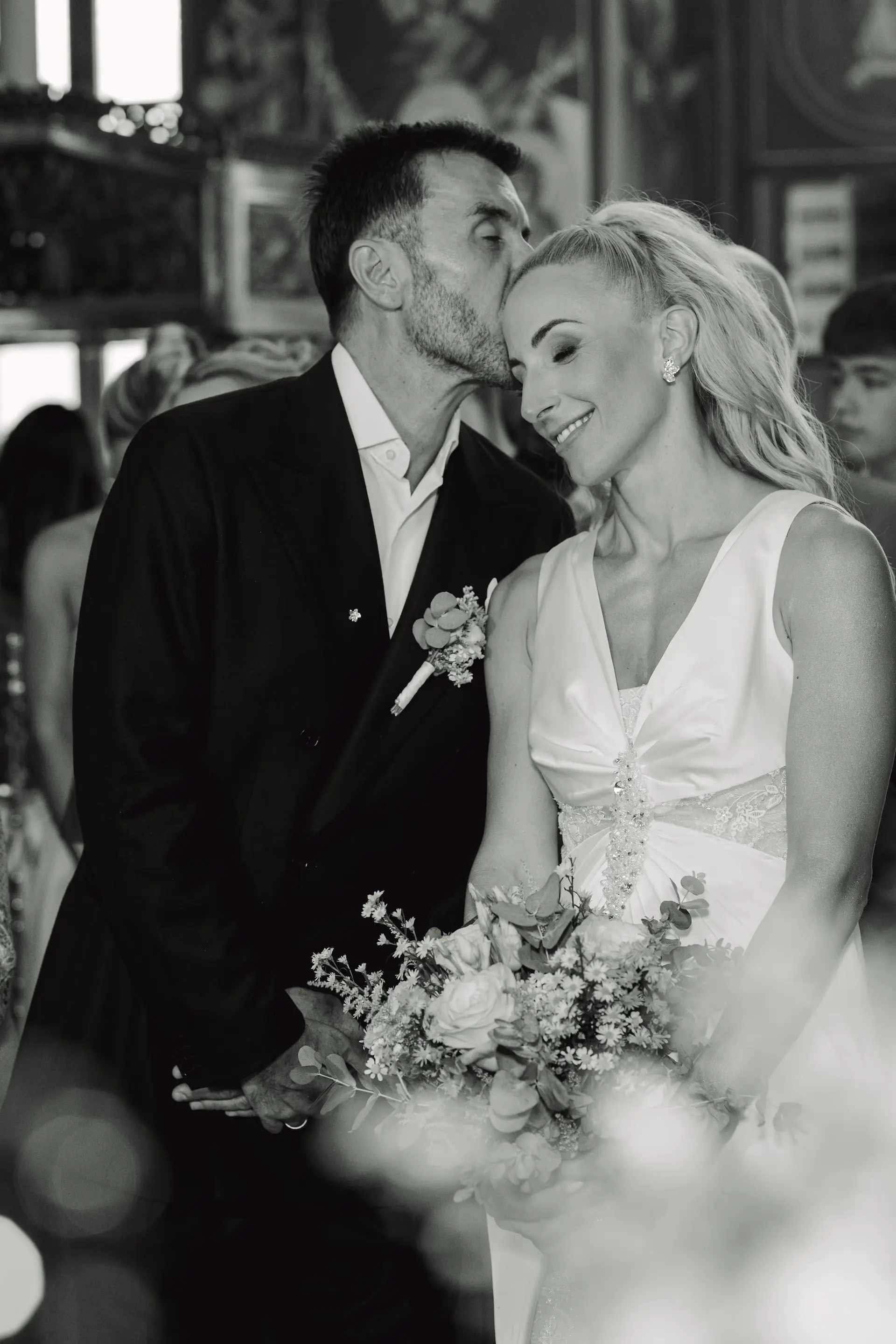 Emotional black and white wedding photography: Groom gently kissing the bride’s forehead in a moment of pure tenderness.