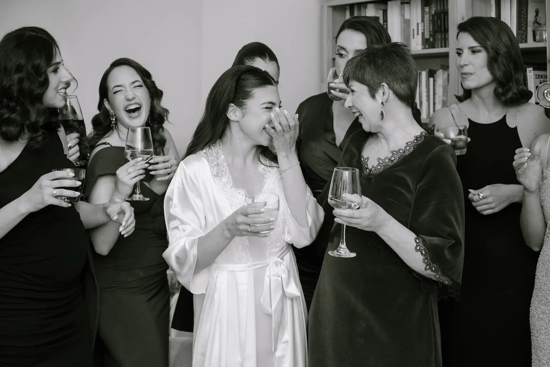a group of women laughing and drinking wine during bride preparation