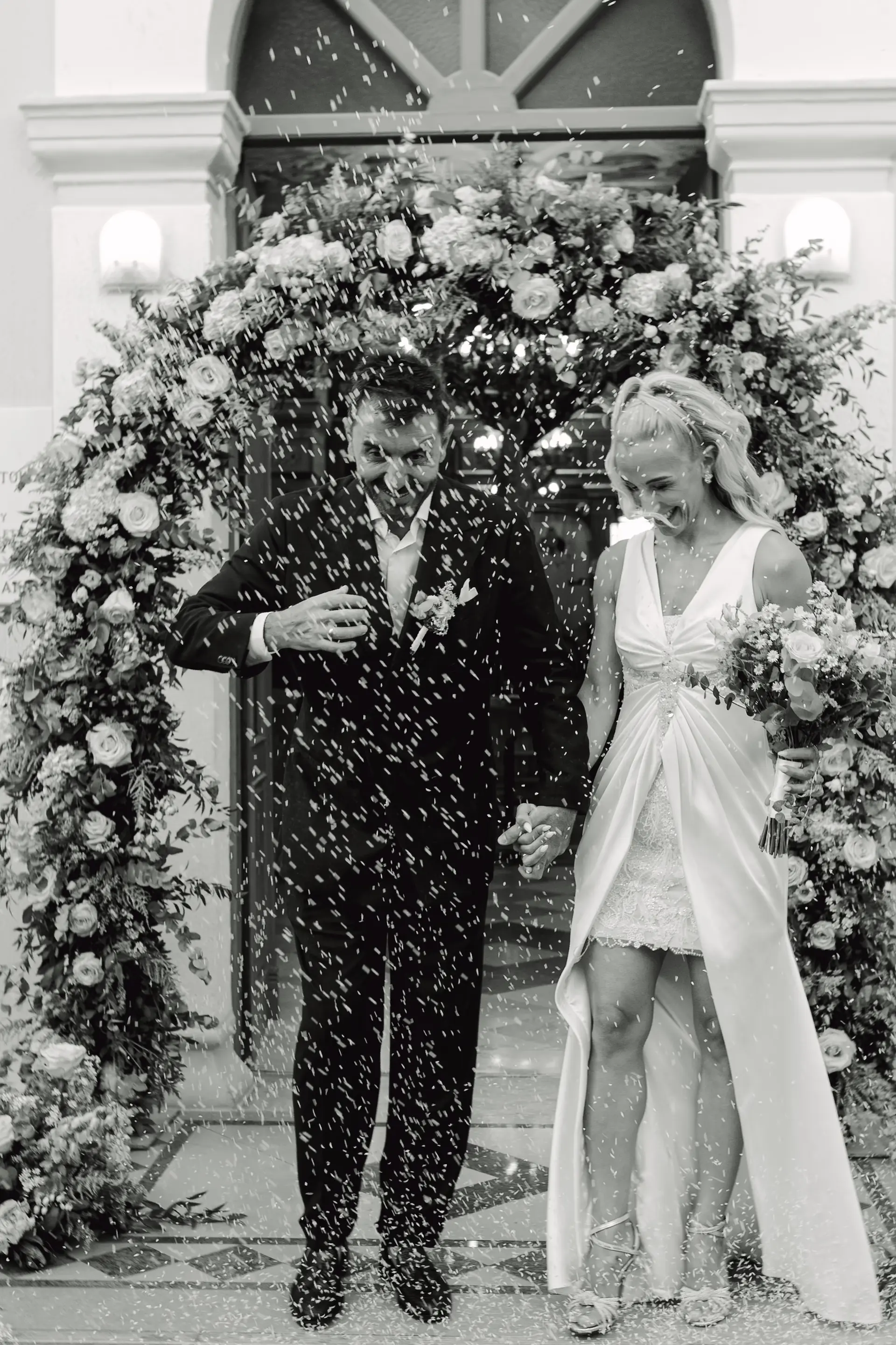 Dynamic black and white wedding photo of the couple exiting the church while guests throw rice, capturing a celebration of pure joy.