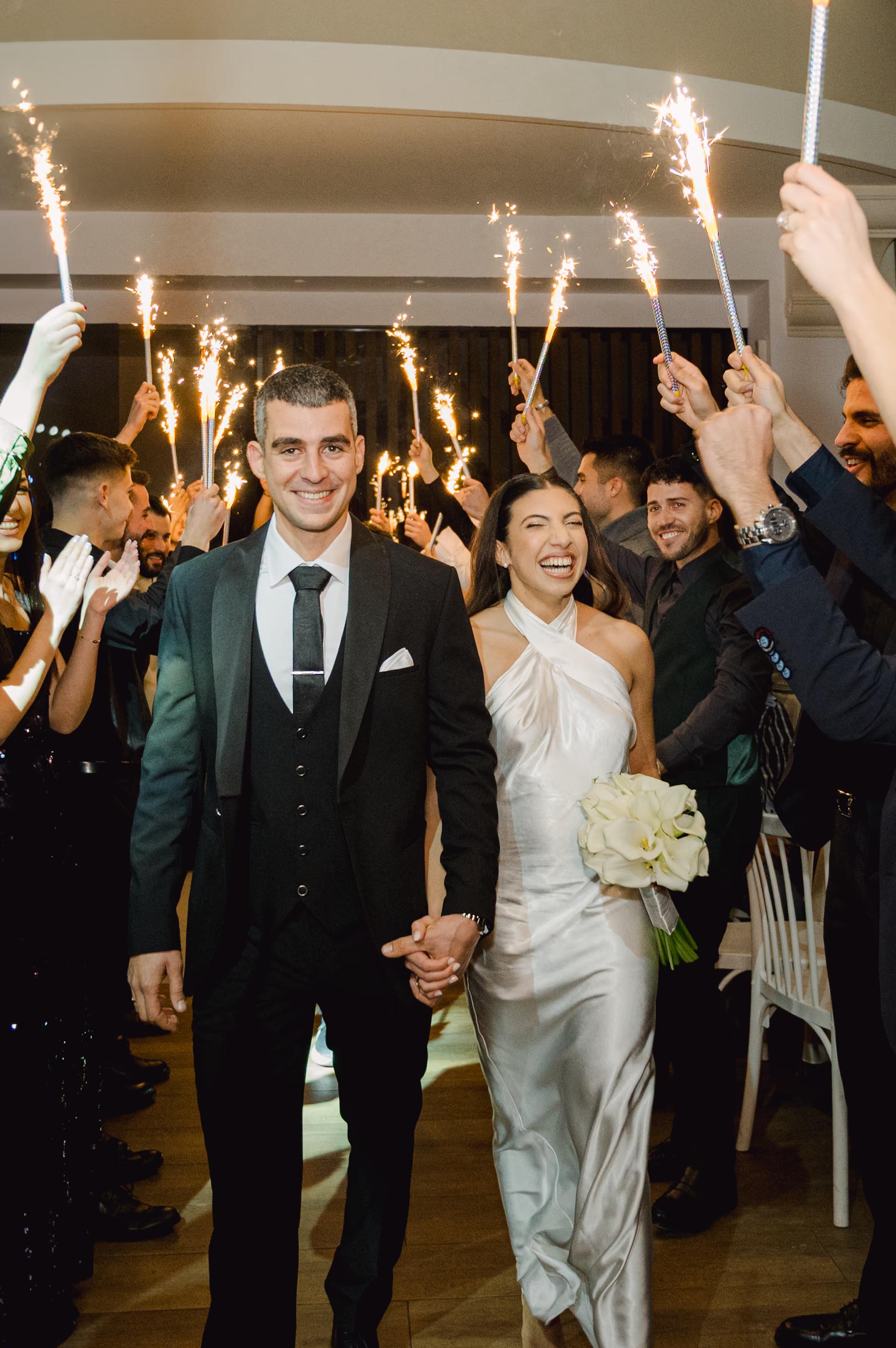 groom and bride holding hands and smiling entering the venue surrounded by friends