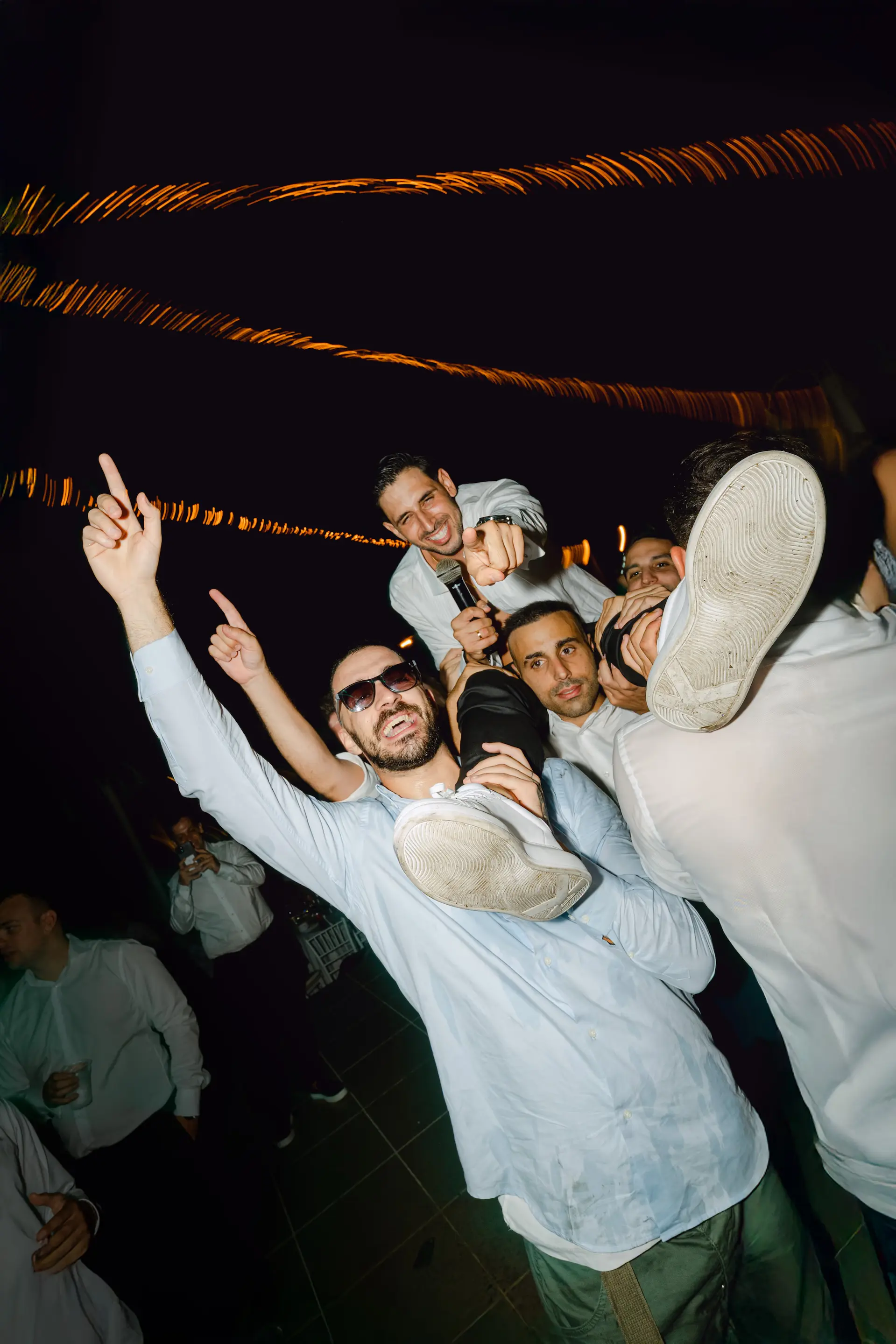 groom is lifted by his friends and points at the camera