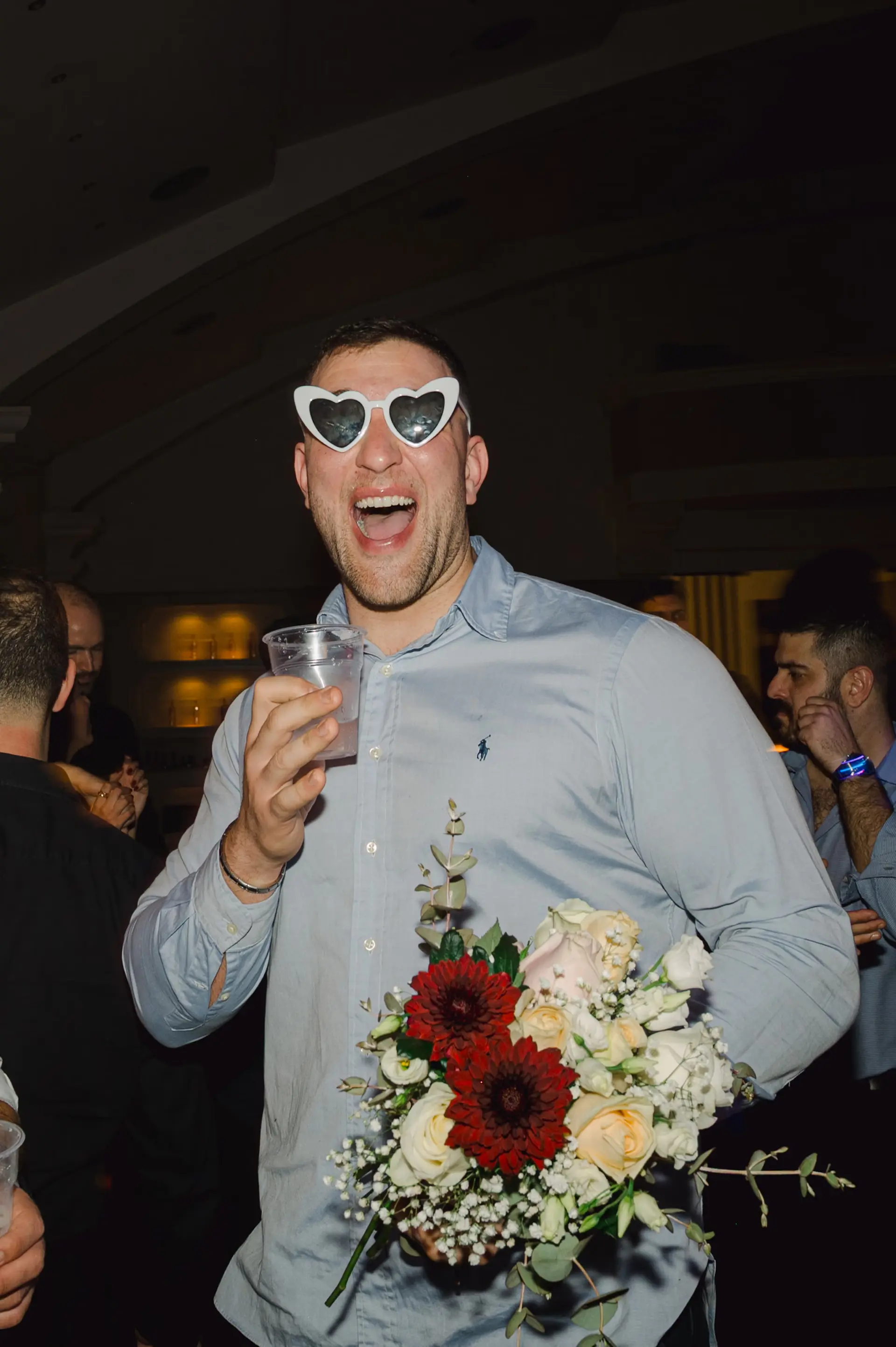 a man holding a drink and the wedding bouquet laughing