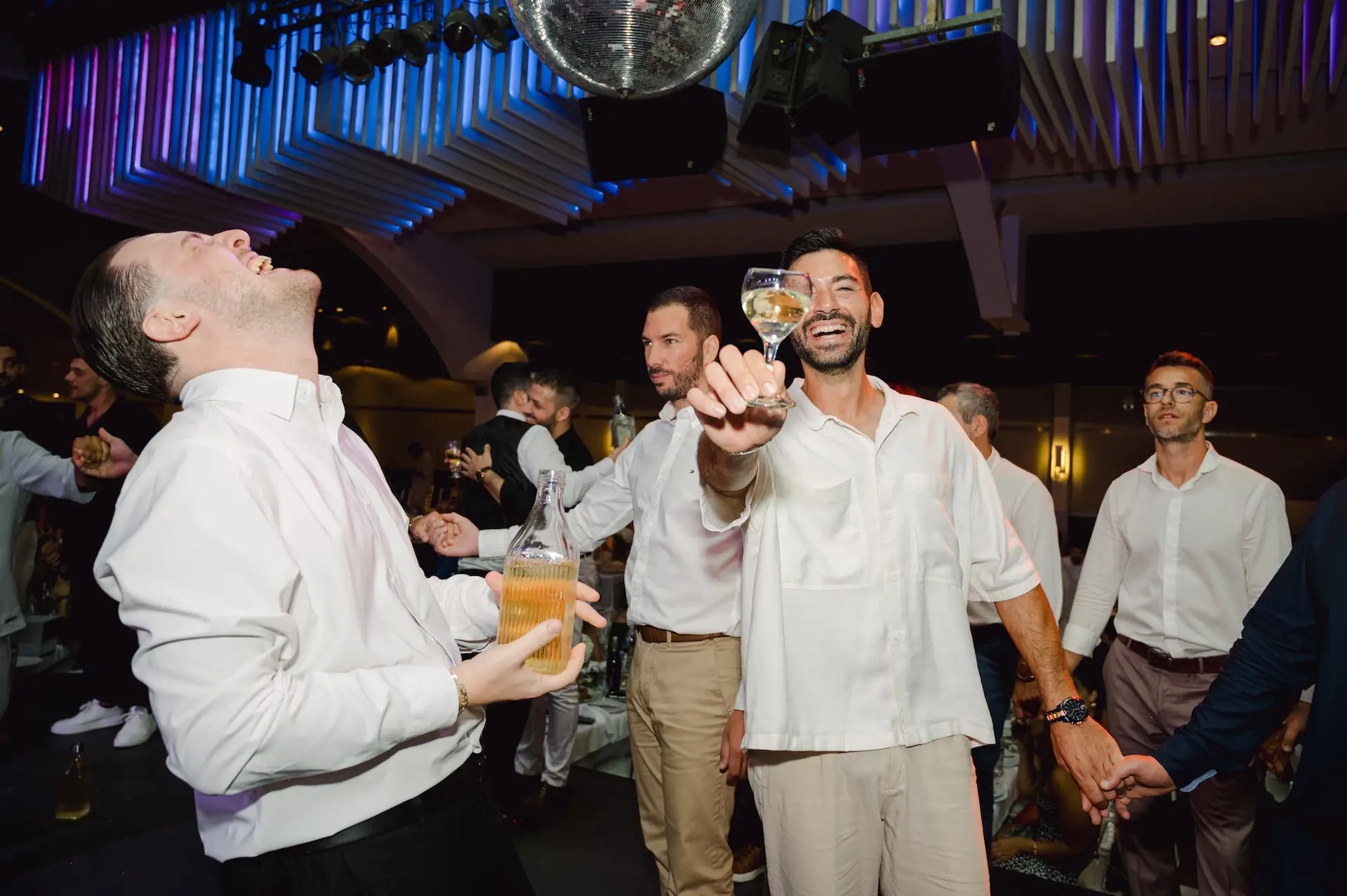 a group of men holding wine glasses and laughing during wedding party