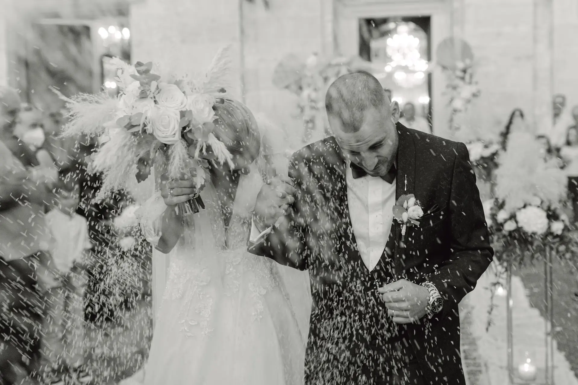 Joyful newlywed couple coming out of the church as guests throw rice to celebrate