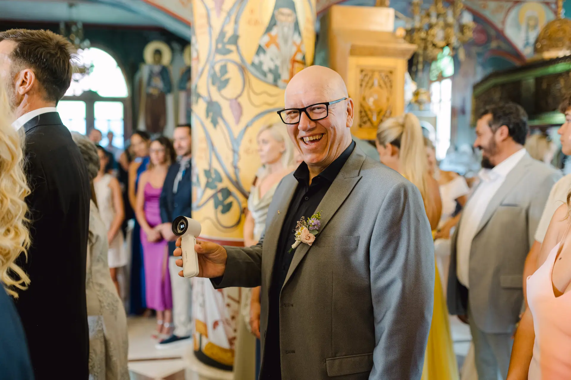 A fun, candid moment during the ceremony: The best man laughing while using a mini fan to cool down the bride and groom