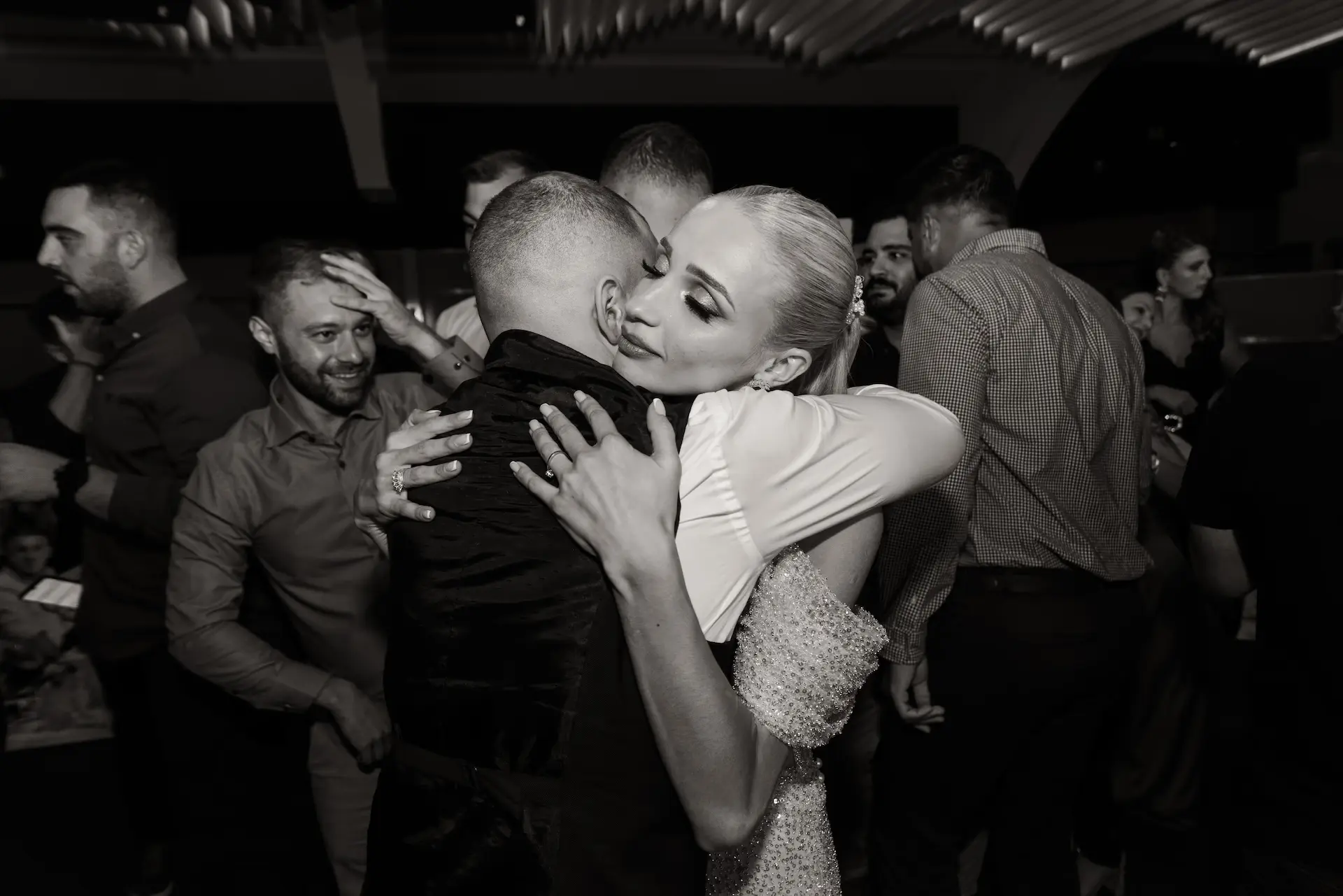 Emotional hug between the couple during their wedding party, captured in a timeless black and white style.