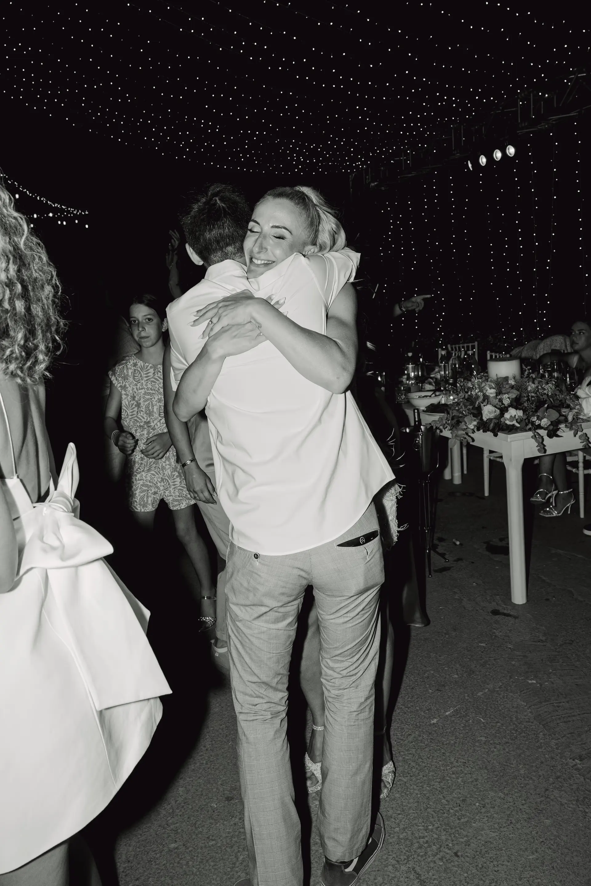 Black and white candid photo of two wedding guests hugging on the dance floor.