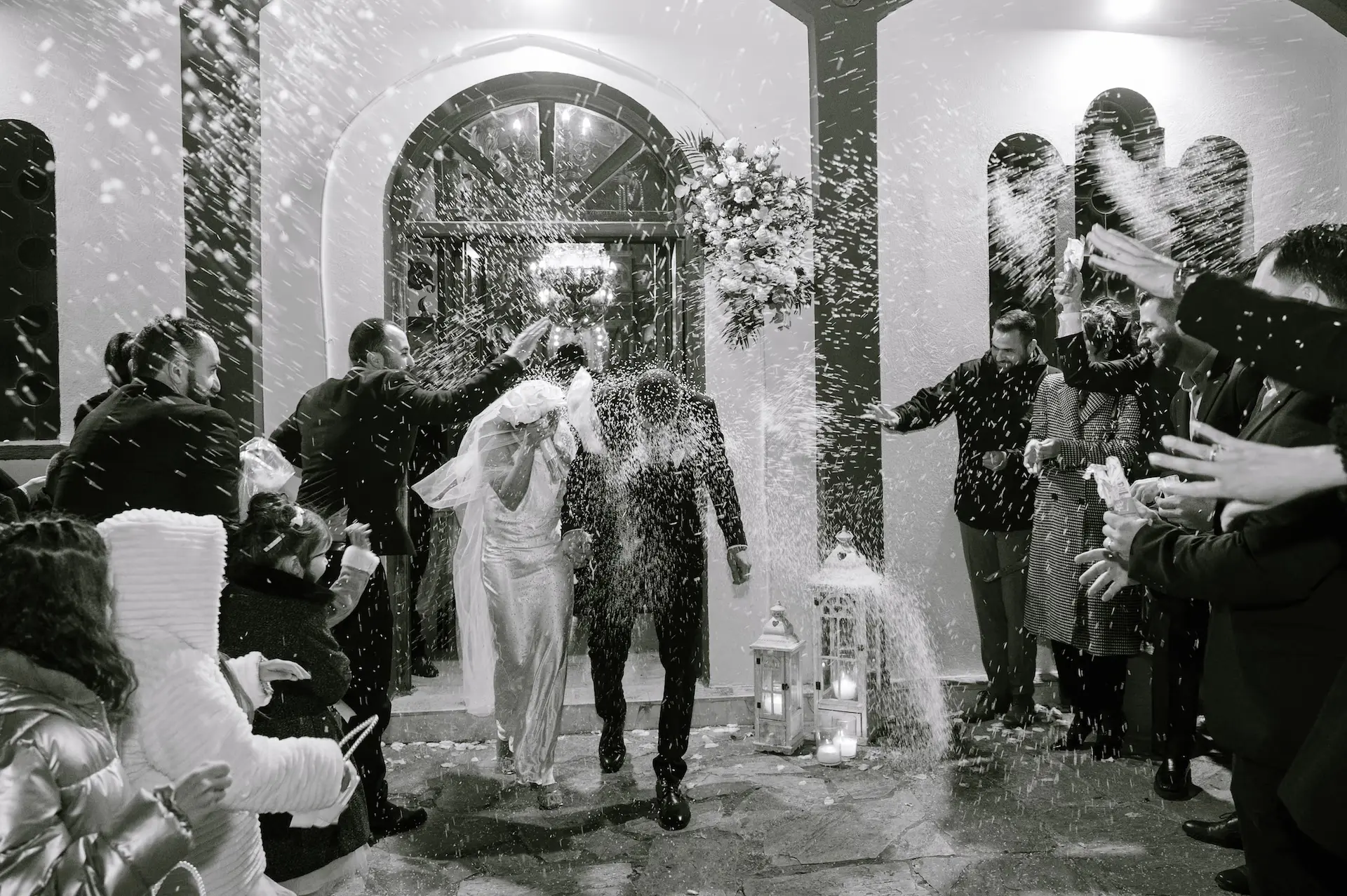Joyful wedding guests throwing rice at the newlywed couple as they exit the stone church.