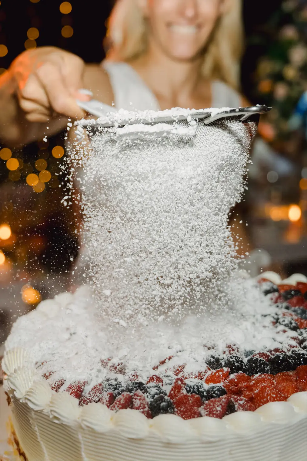 A sweet and candid moment as the bride adds the finishing touch of sugar to her fruit-filled wedding cake close up