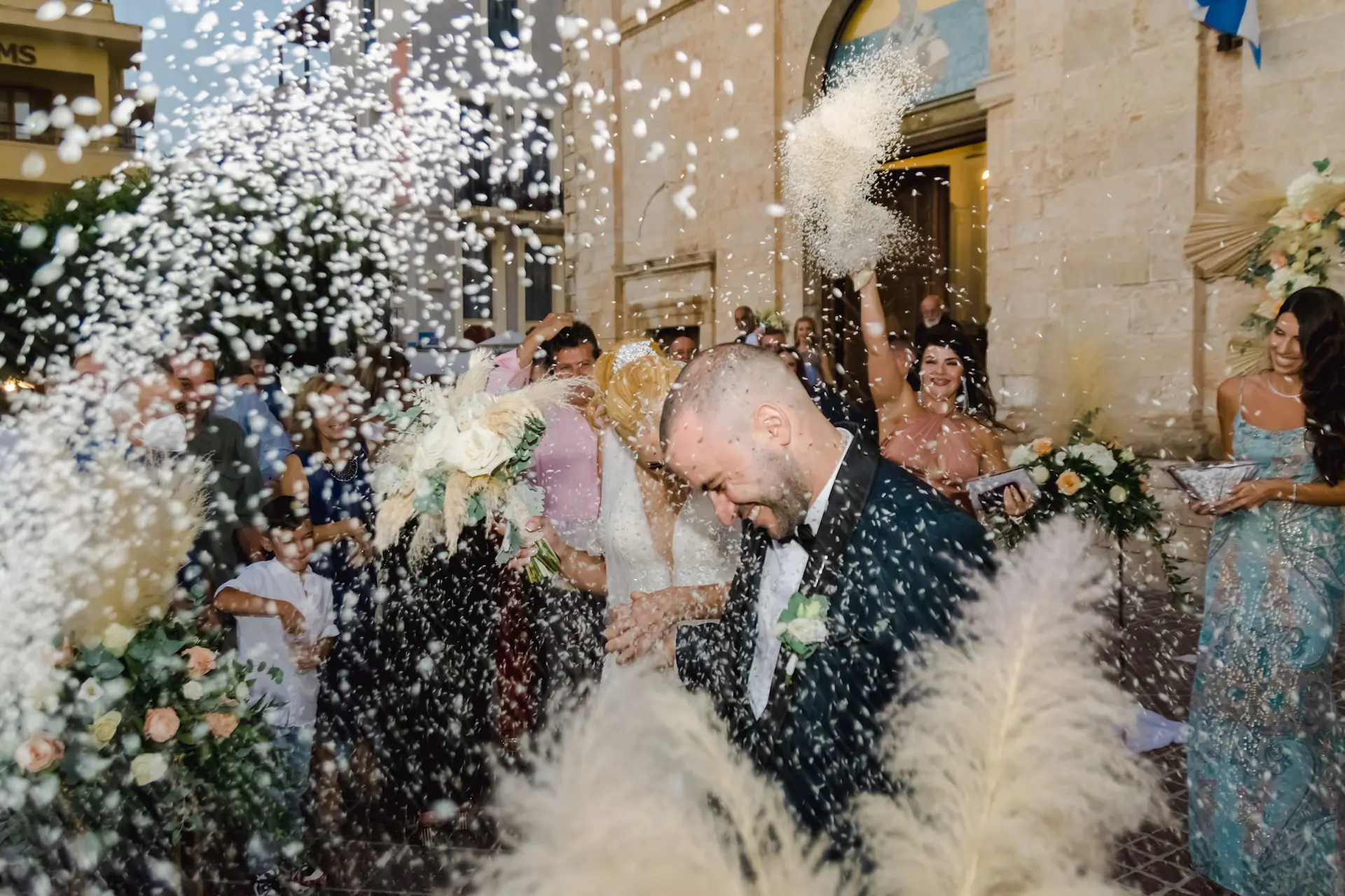 Joyful newlywed couple coming out of the church as guests throw rice to celebrate