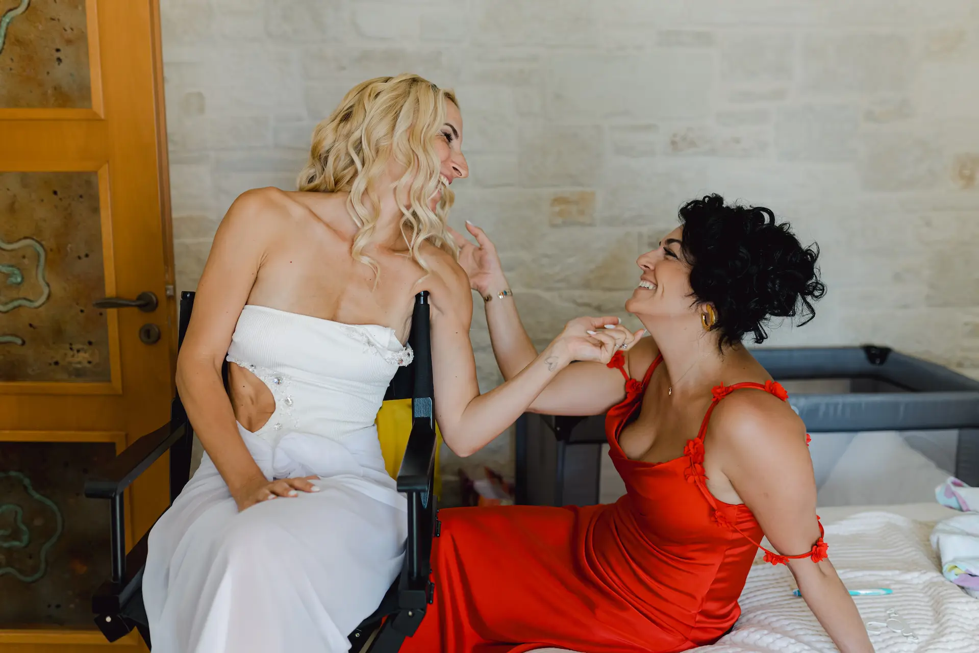 bride and her best griend sitting on a bed during her make up preparations