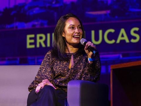 A guest smiles and speaks into a microphone, her name projected on the screen behind her.