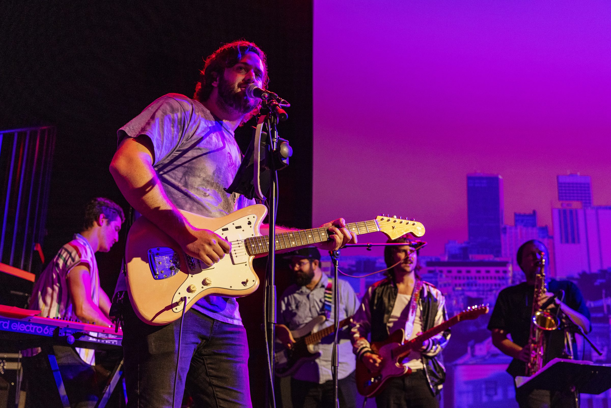 A band plays on a purple-lit stage in front of a projected Oklahoma City skyline.