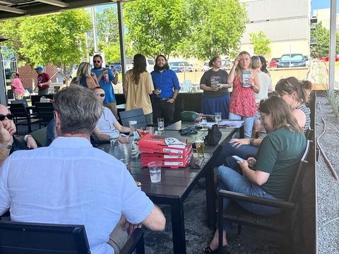 Guests sit around patio tables with pizza boxes while others stand and talk.