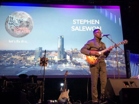A guitarist performs on stage in front of a screen showing The Election Night Show at the Tower Theatre graphic.