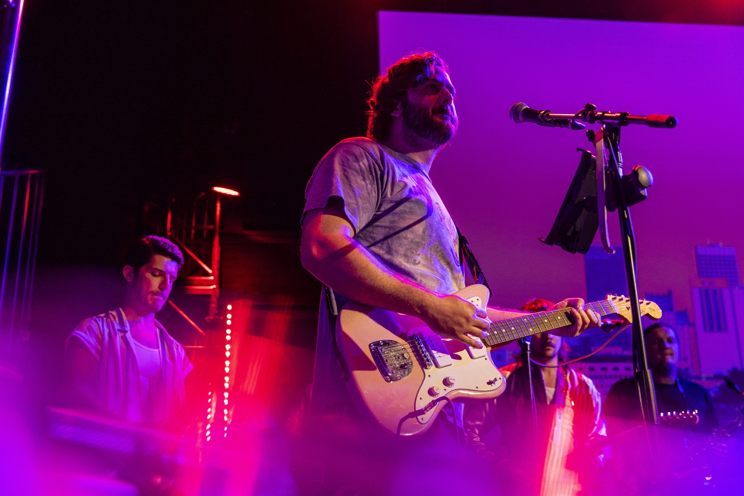 A guitarist leans into the microphone mid-song, lit in magenta.