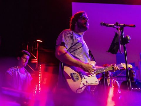 A guitarist leans into the microphone mid-song, lit in magenta.