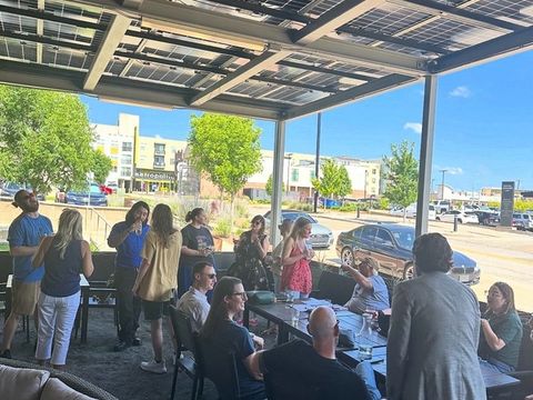 People gather and chat under a solar-panel patio canopy on a sunny afternoon.