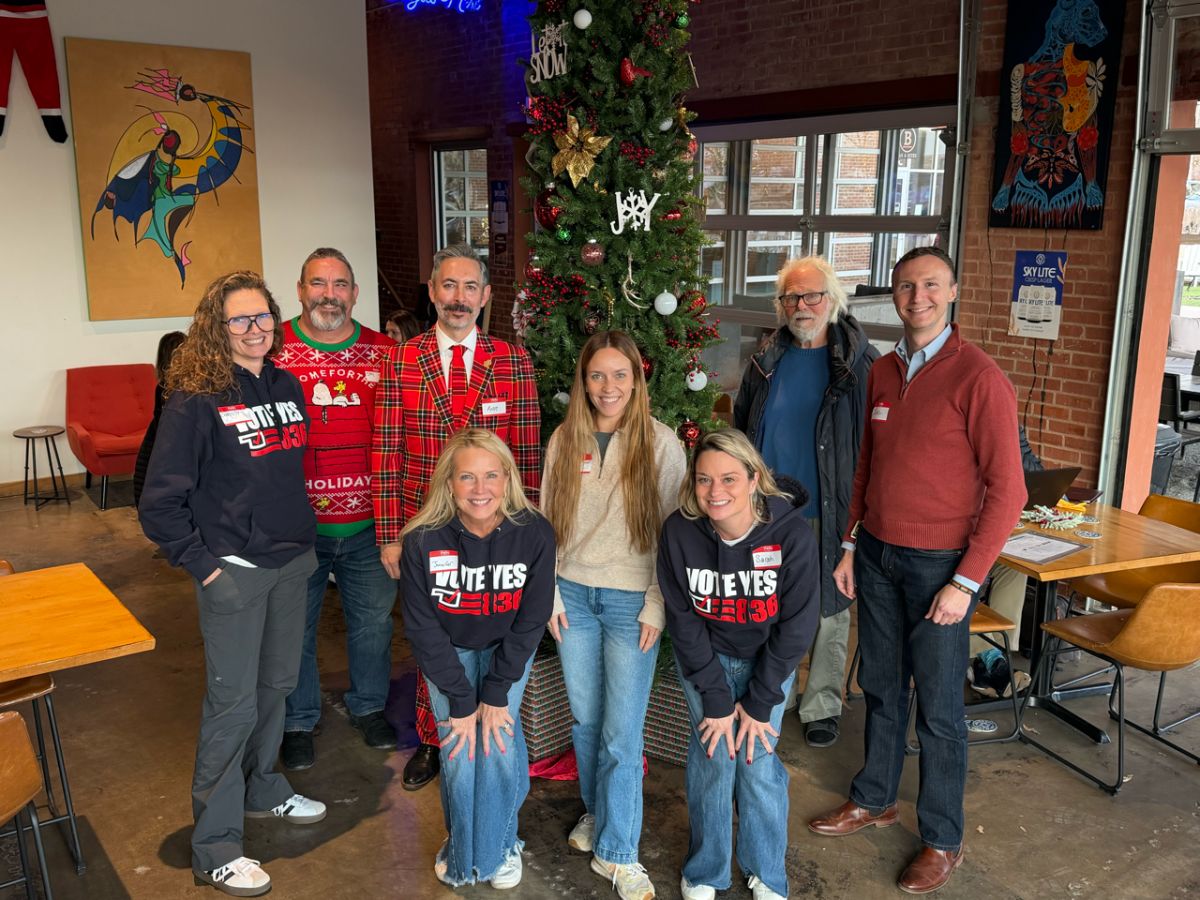 Nine people pose together in front of a Christmas tree at a holiday gathering.