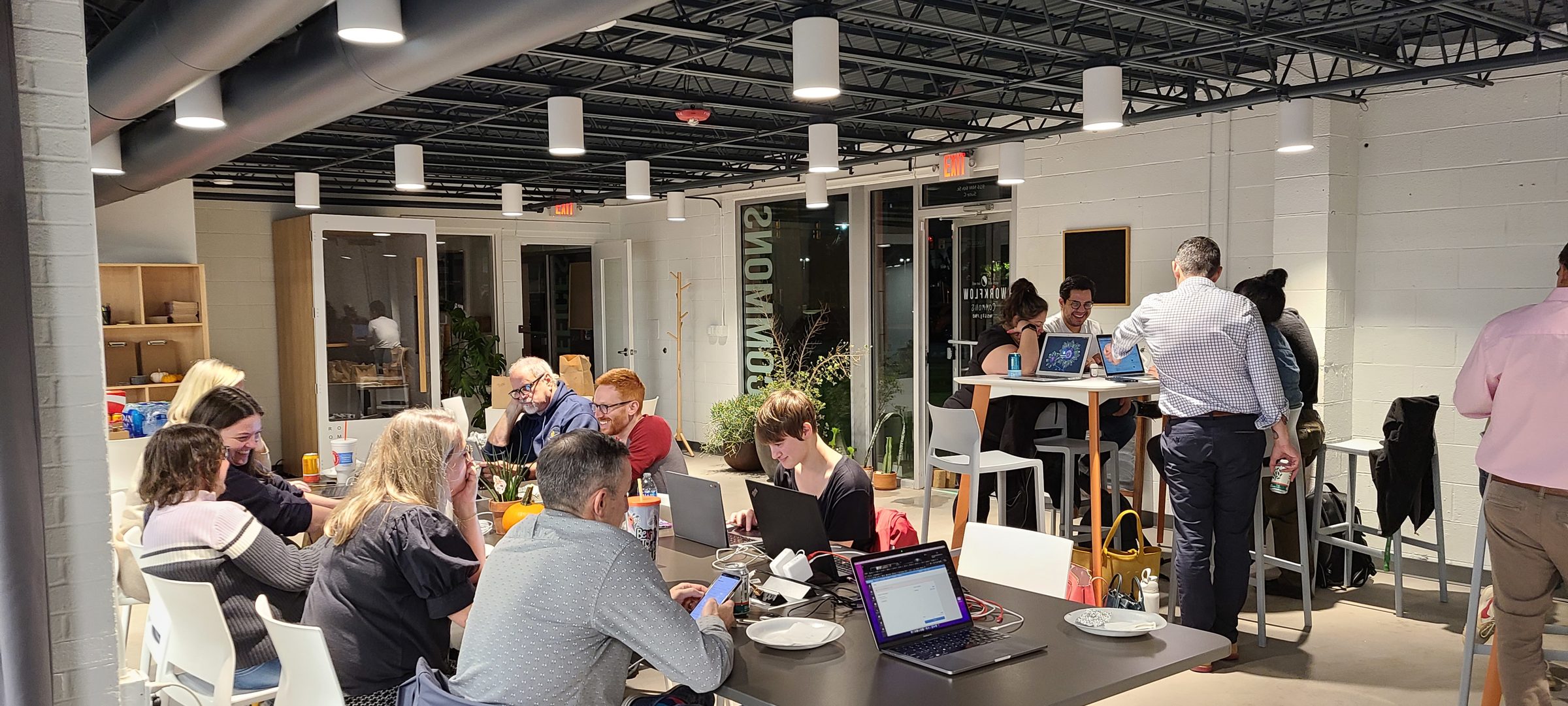 Volunteers work on laptops and phones around tables during an evening text-banking session.
