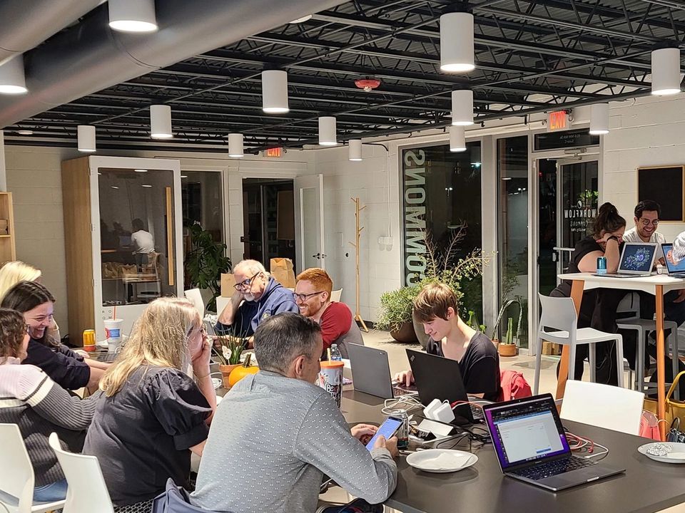 Volunteers work on laptops and phones around tables during an evening text-banking session.