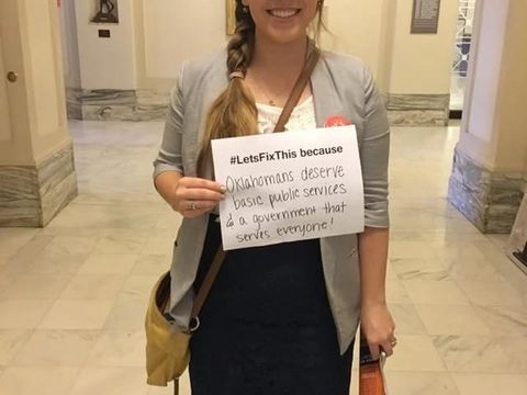 A woman in the Capitol holds a handwritten "#LetsFixThis because" sign.