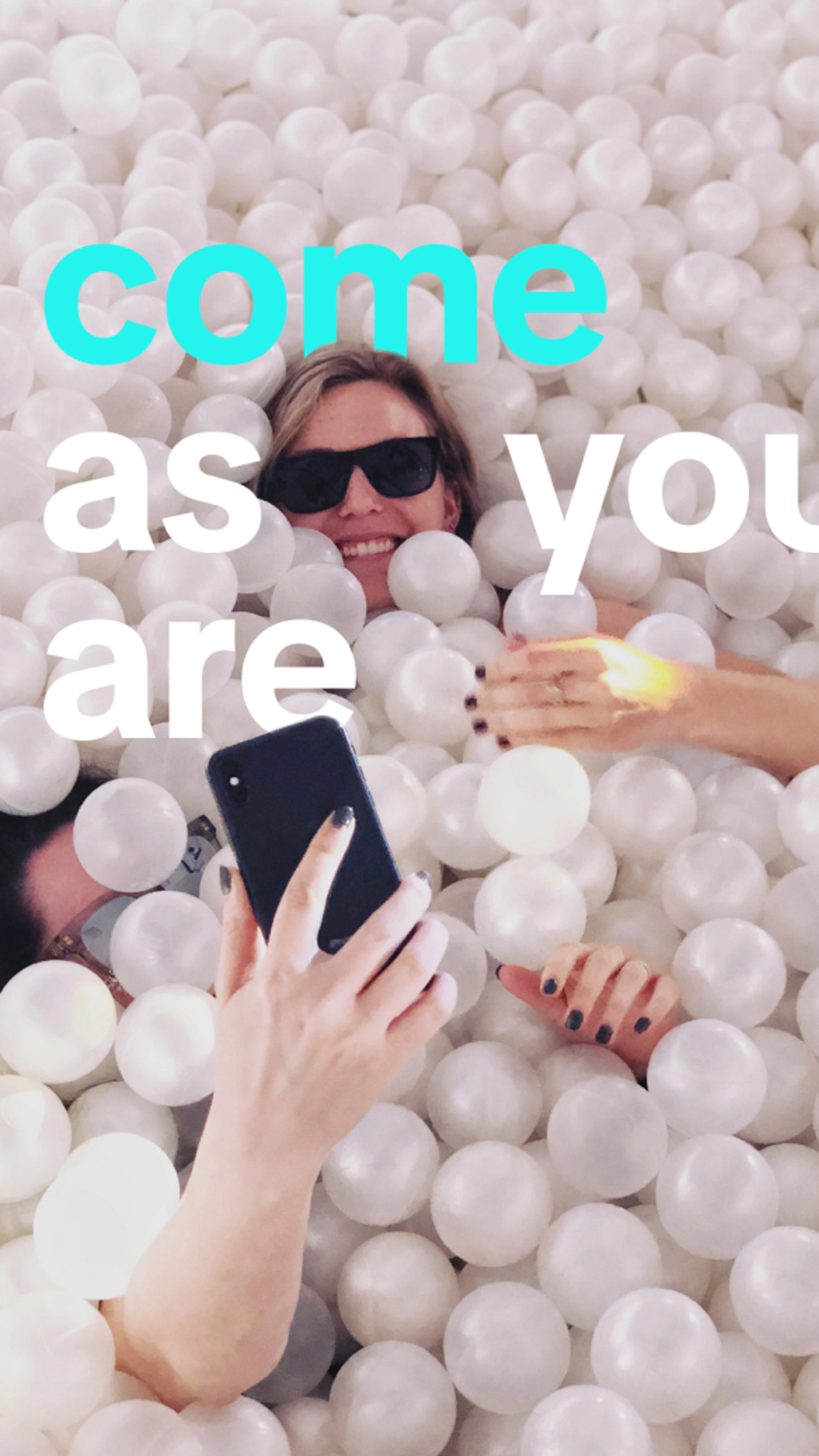 A smiling female TikTok employee submerged in a plastic balls pit holds up her phone to take a selfie.