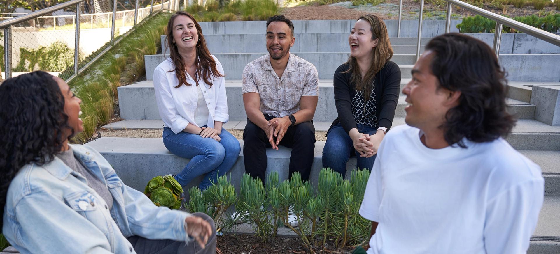 A diverse group of TikTok employees sitting outside laughing