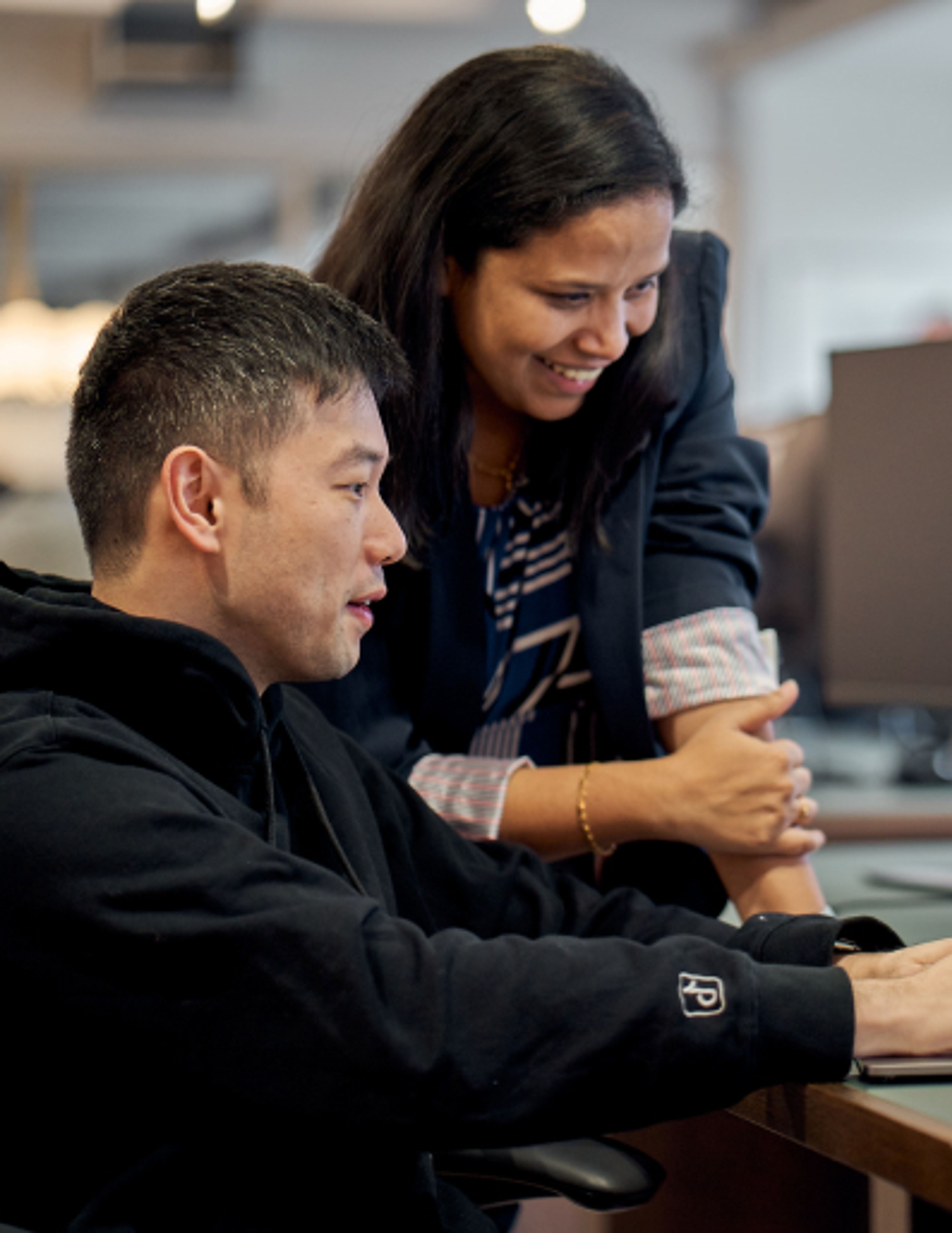 A young male and a female TikTok employee smile as they work on a project together.