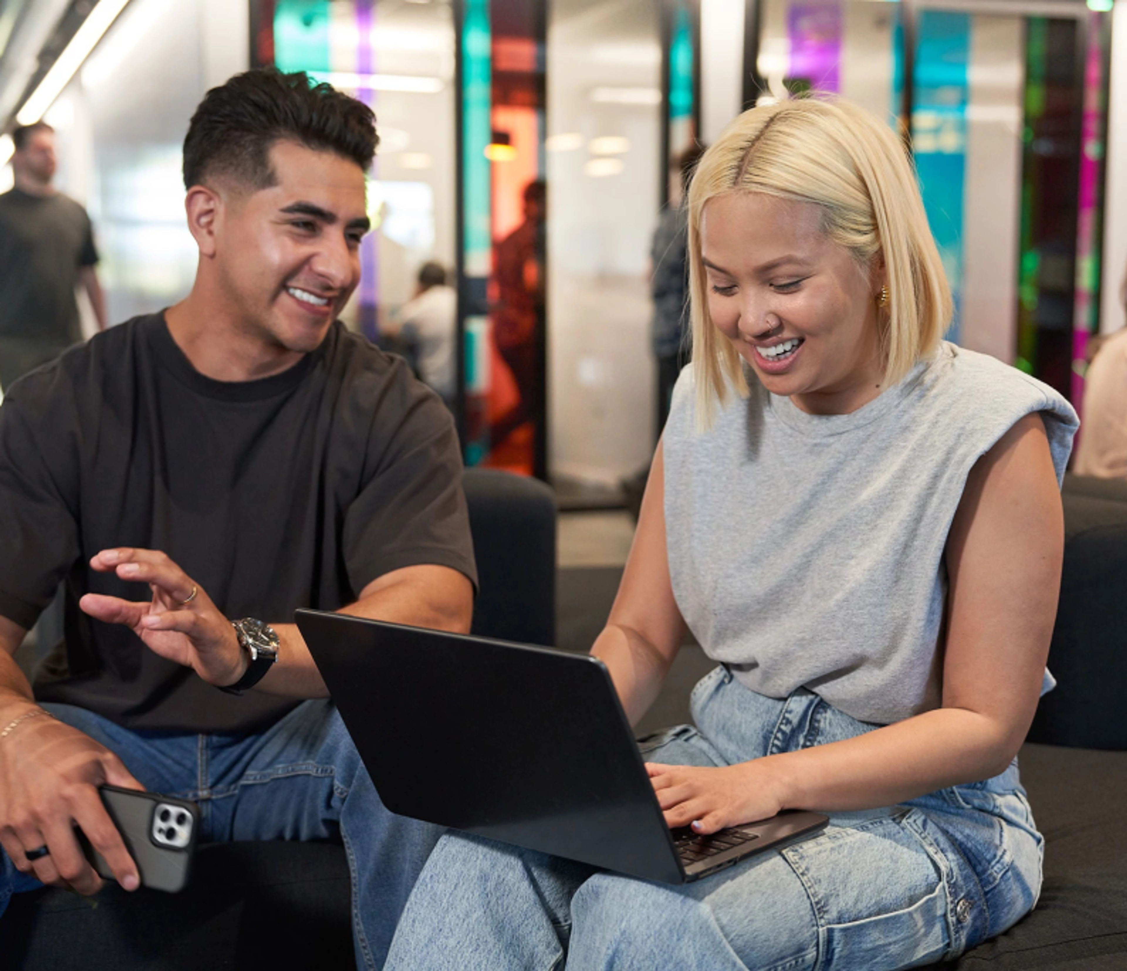 A male and a female TikTok employee sit beside each other as they talk and work on a project on a laptop.