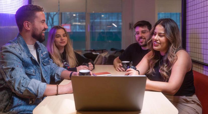 Four TikTok Latin America Working Student Program attendees sit at a desk and look at the screen of an open laptop.