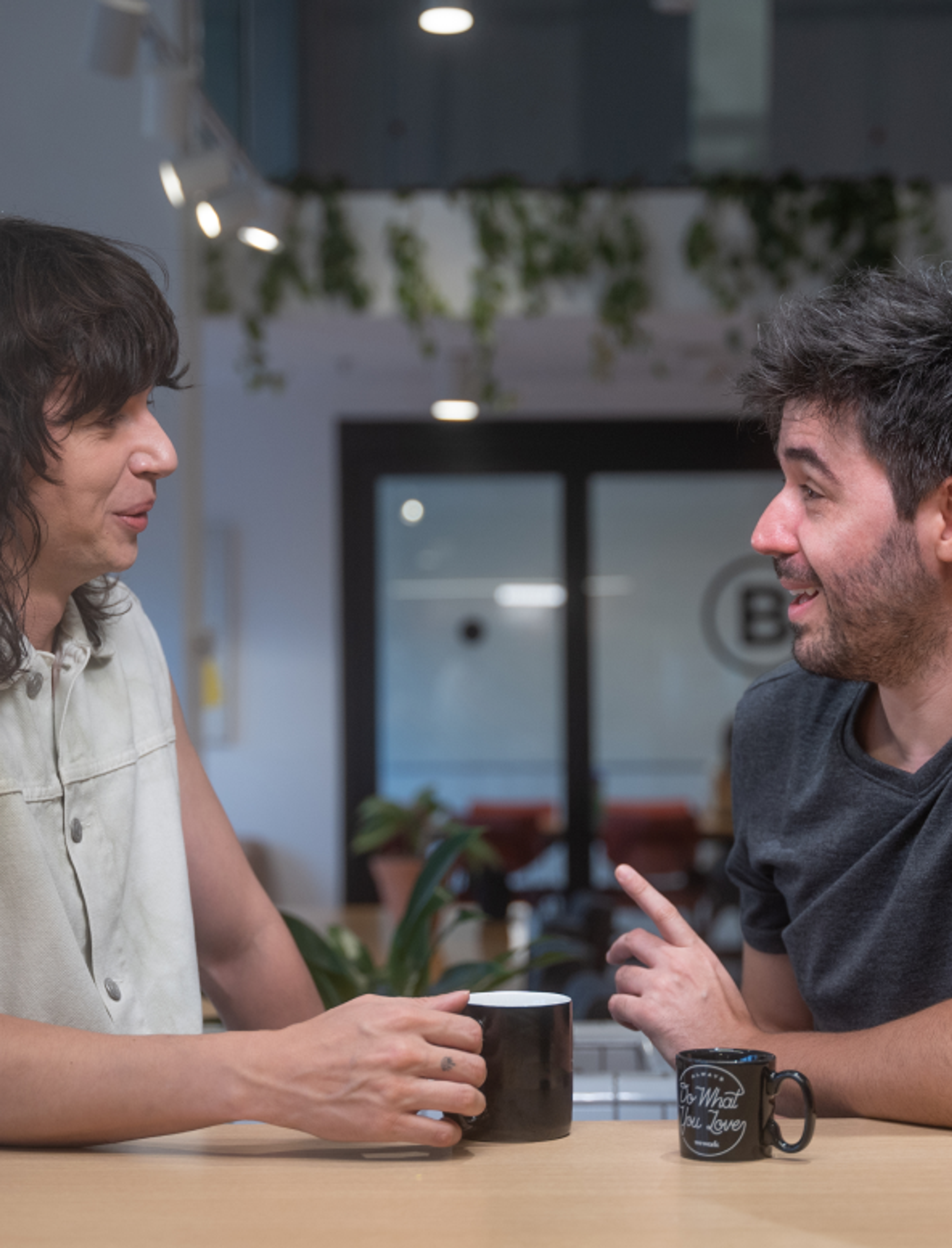 Two young male ByteDance employees smile and laugh as they sit having coffee together.