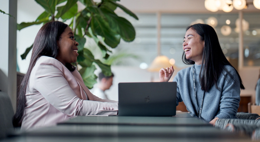 Two female TikTok Working Student Program participants sit next to an open laptop as they work together.