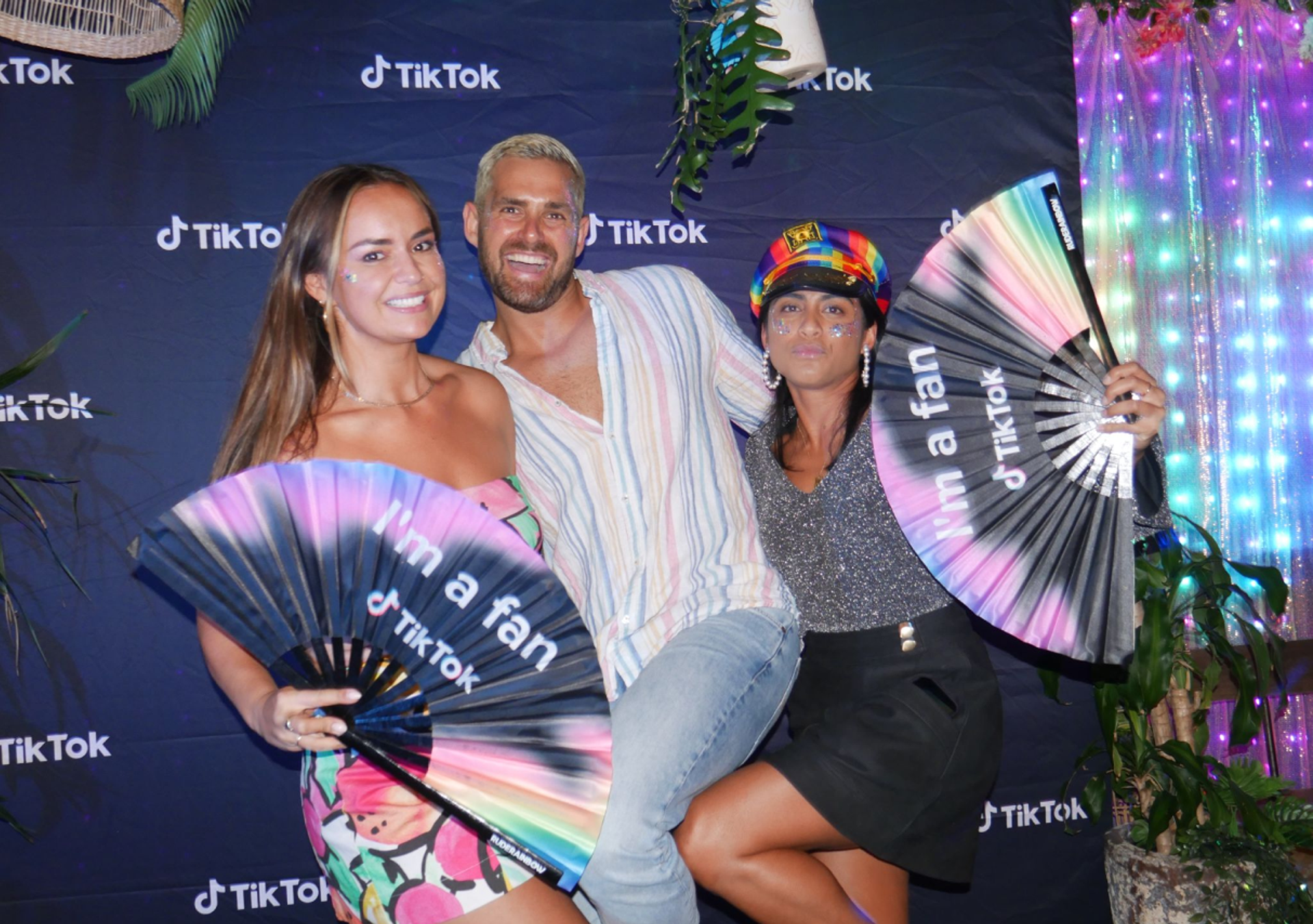 Three TikTok employees pose together holding fans at an LGBTQ pride event.