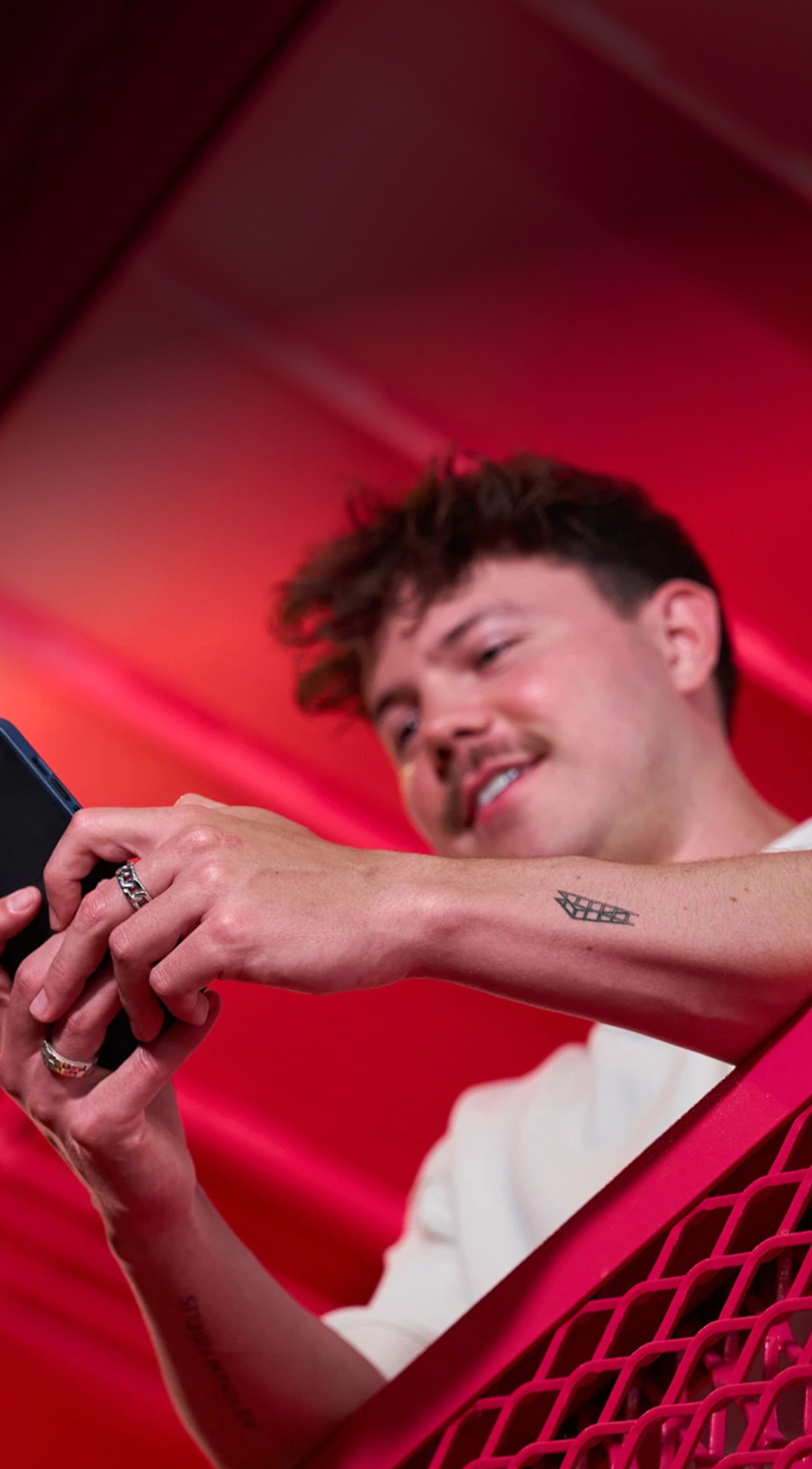 A male TikTok employee with a mustache smiles as he looks at his phone screen.