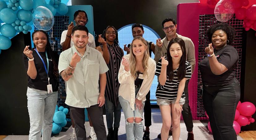 A diverse group of TikTok MBA Interns snap their fingers as they pose for a picture together.