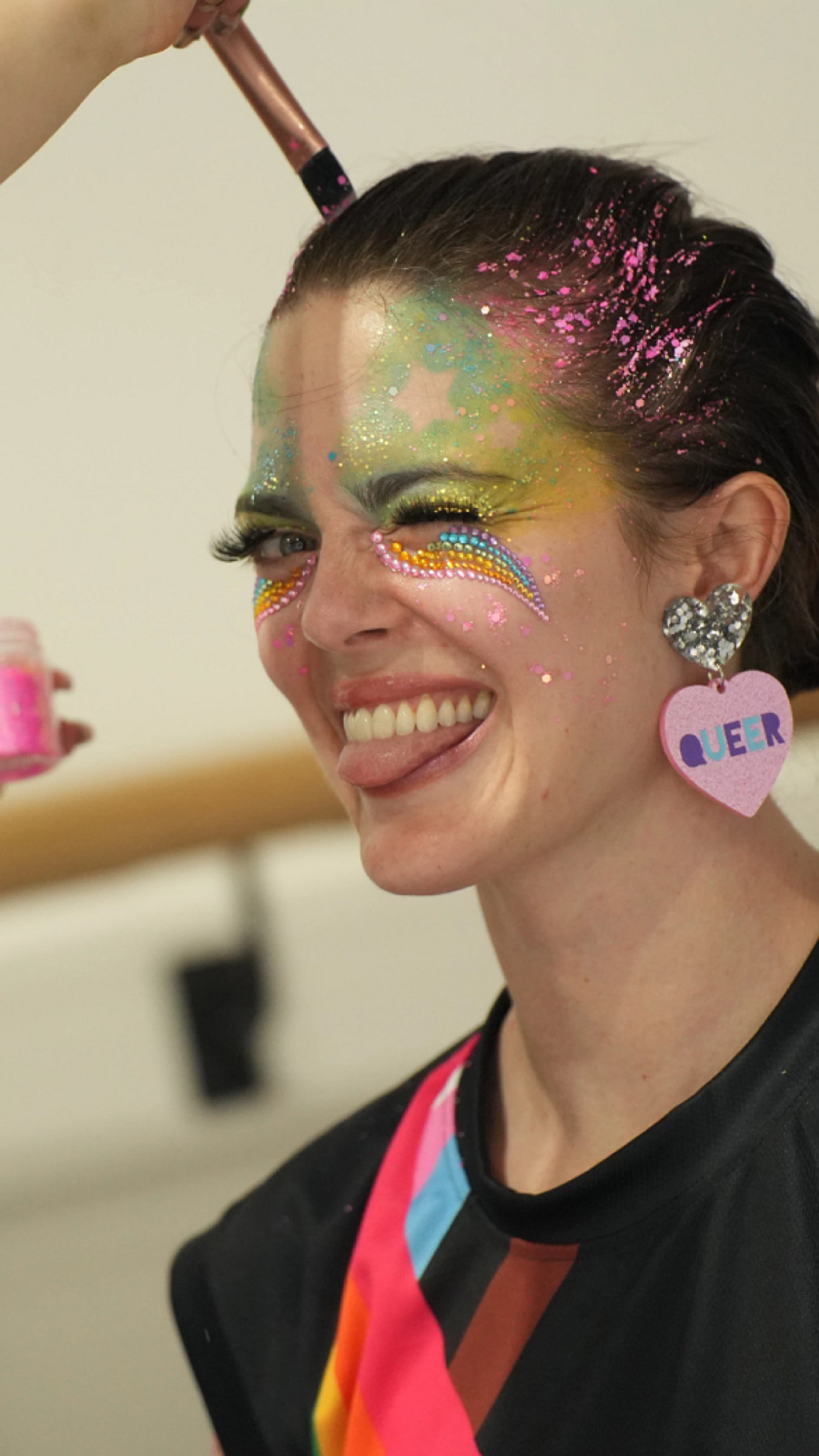 A female TikTok employee with glitter on her face and hair smiles and pokes her tongue out as she poses for a picture.