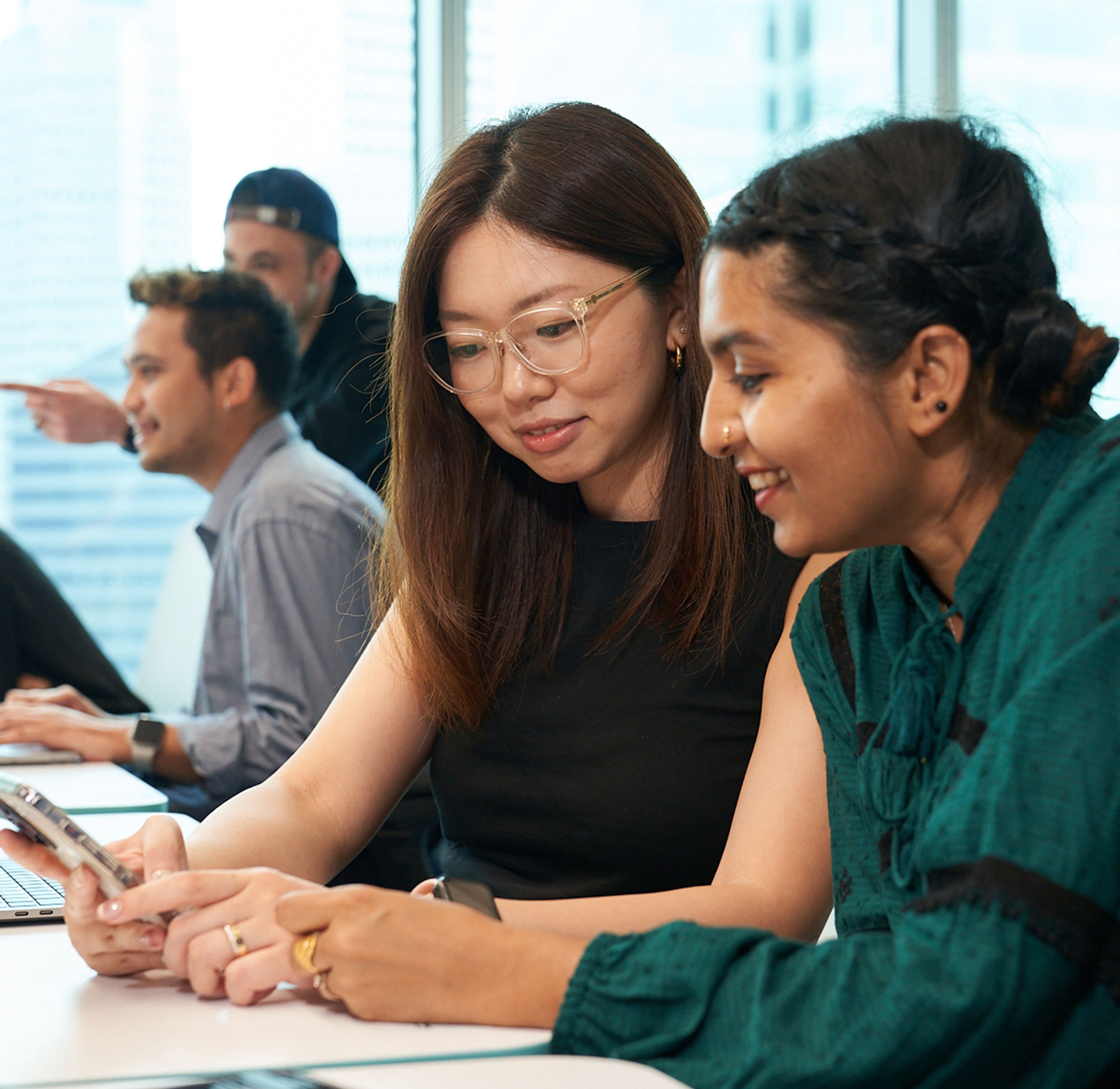 A female ByteDance employee looks at a mobile device of another female employee.