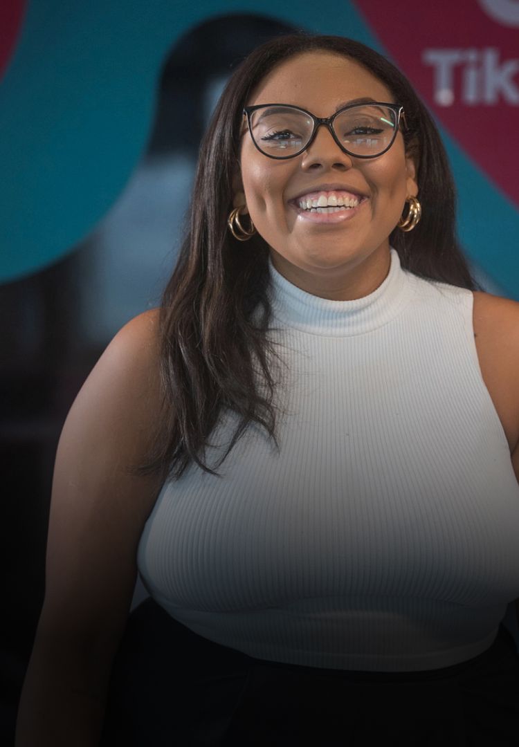 A young black female TikTok employee with glasses smiles as she poses for a picture.