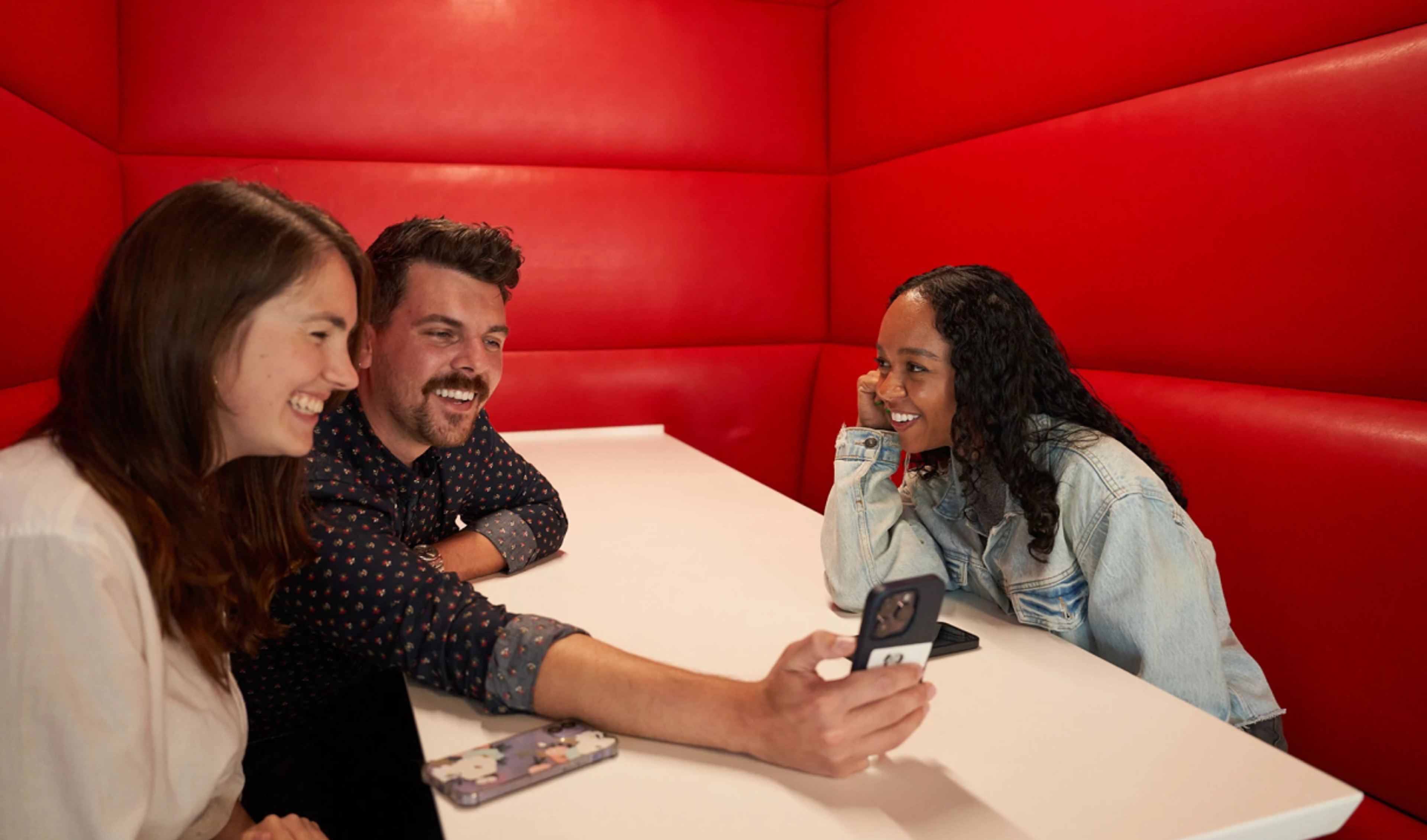 Three young TikTok employees sit together and look at the screen of a smartphone that one of them is holding.