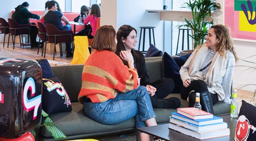 Three TikTok female employees sit on a couch as they talk amongst themselves in the office..