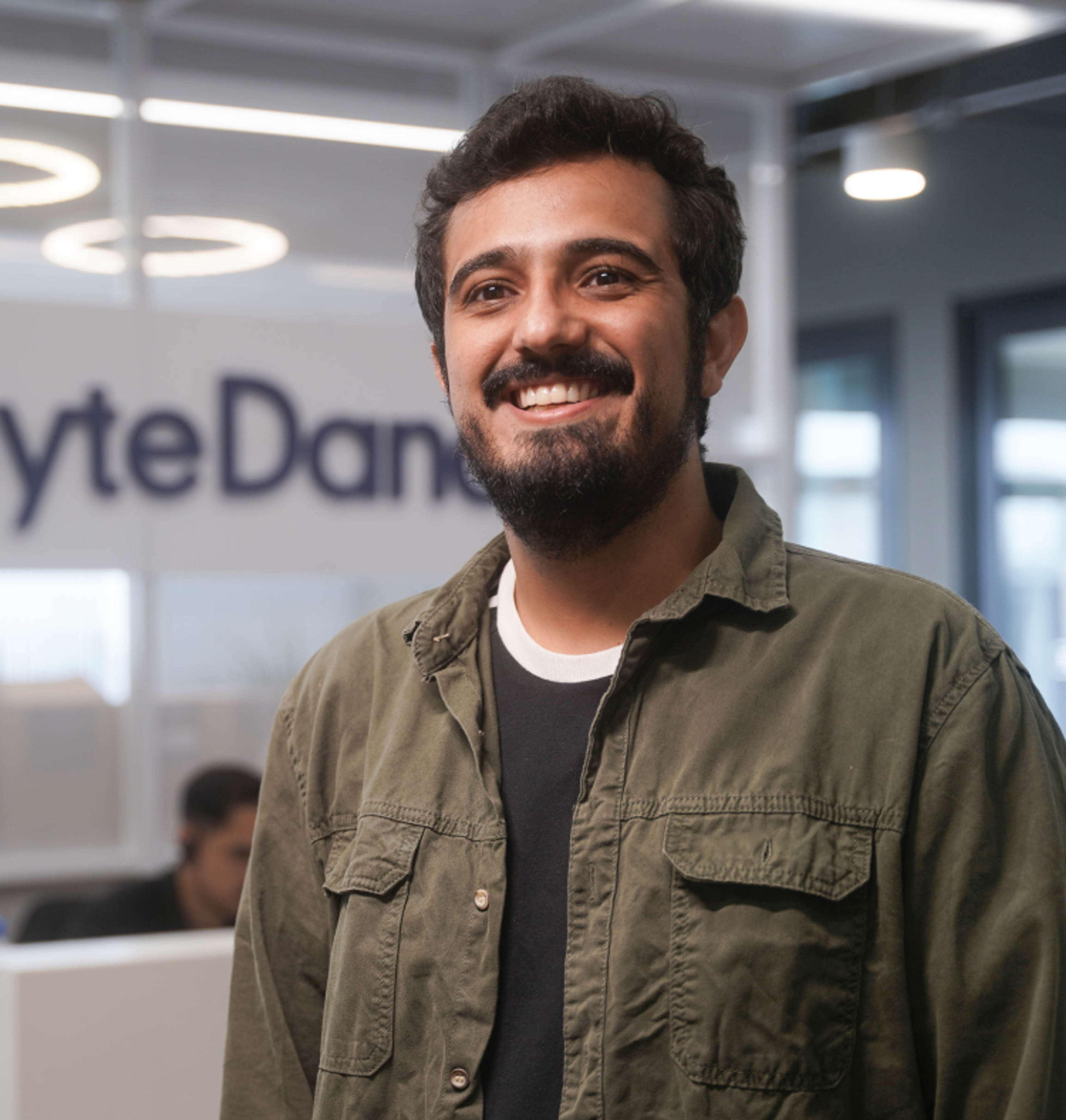 A young male ByteDance employee stands in a ByteDance office and smiles.