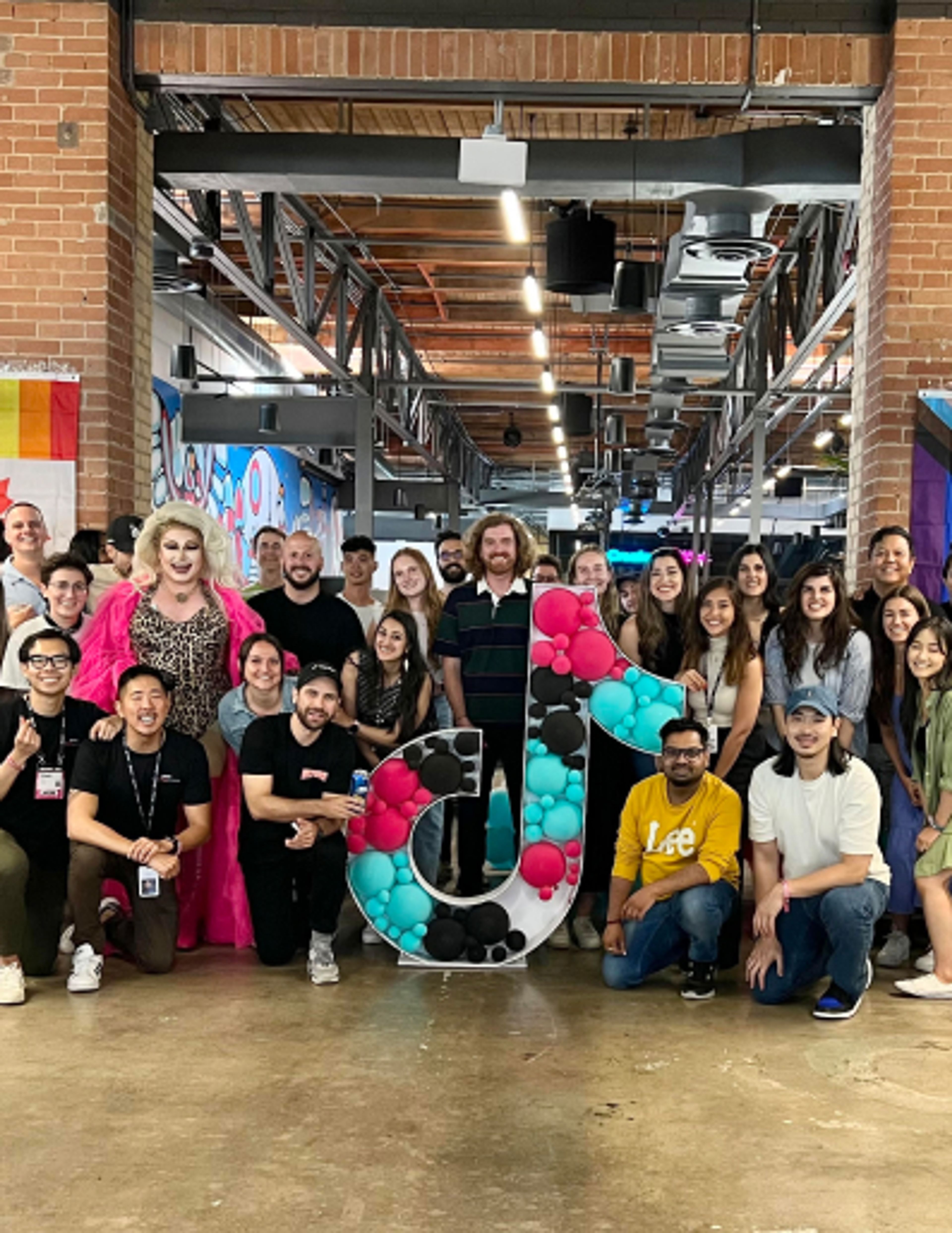 A group of TikTok employees gather around the TikTok music note logo for a photo.