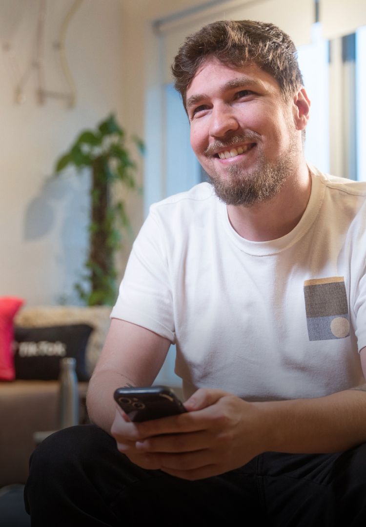 A young white male TikTok employee with a beard smiles and holds a smartphone.