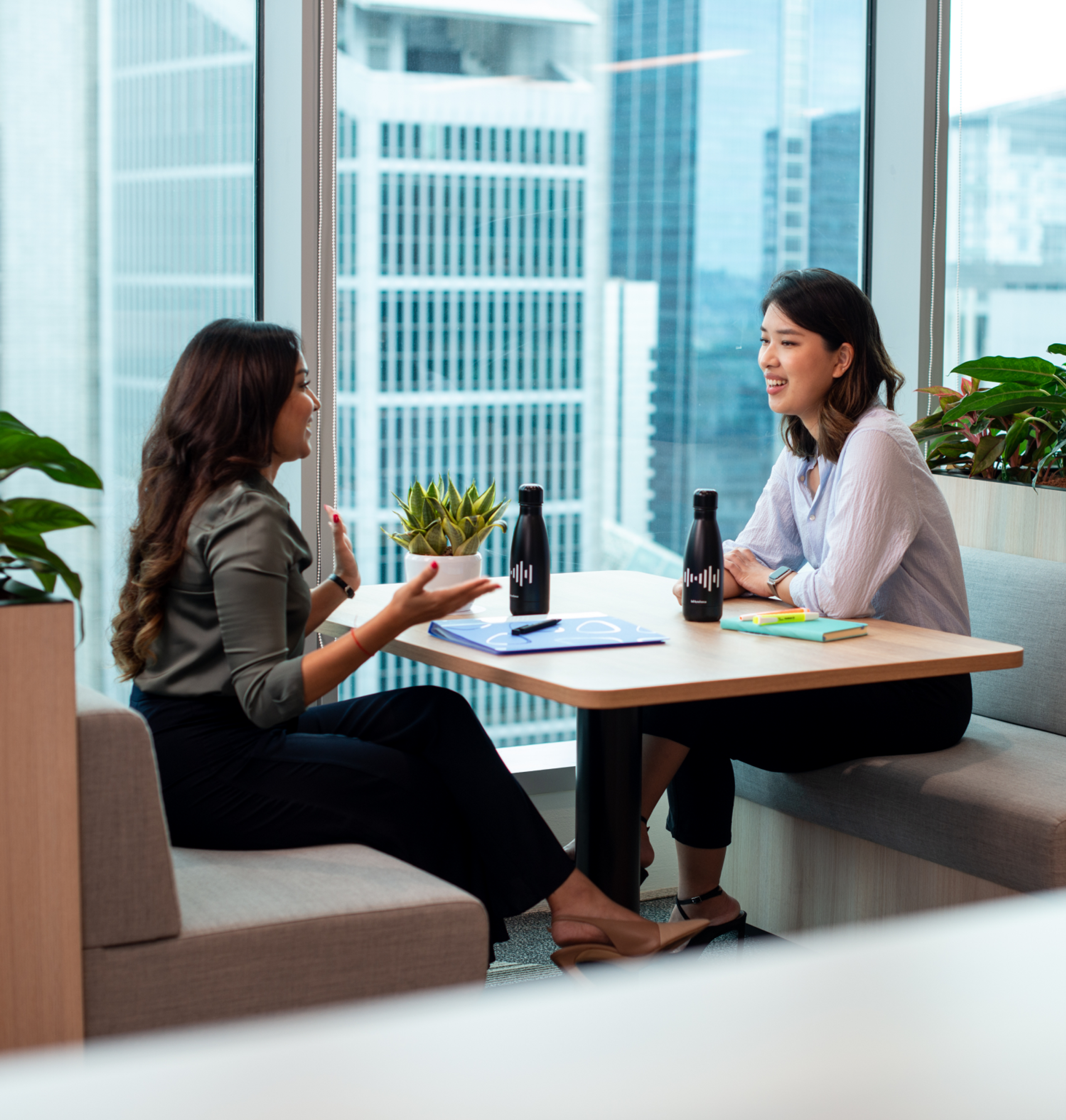 Two young female ByteDance employees sit at a table and discuss a work project.