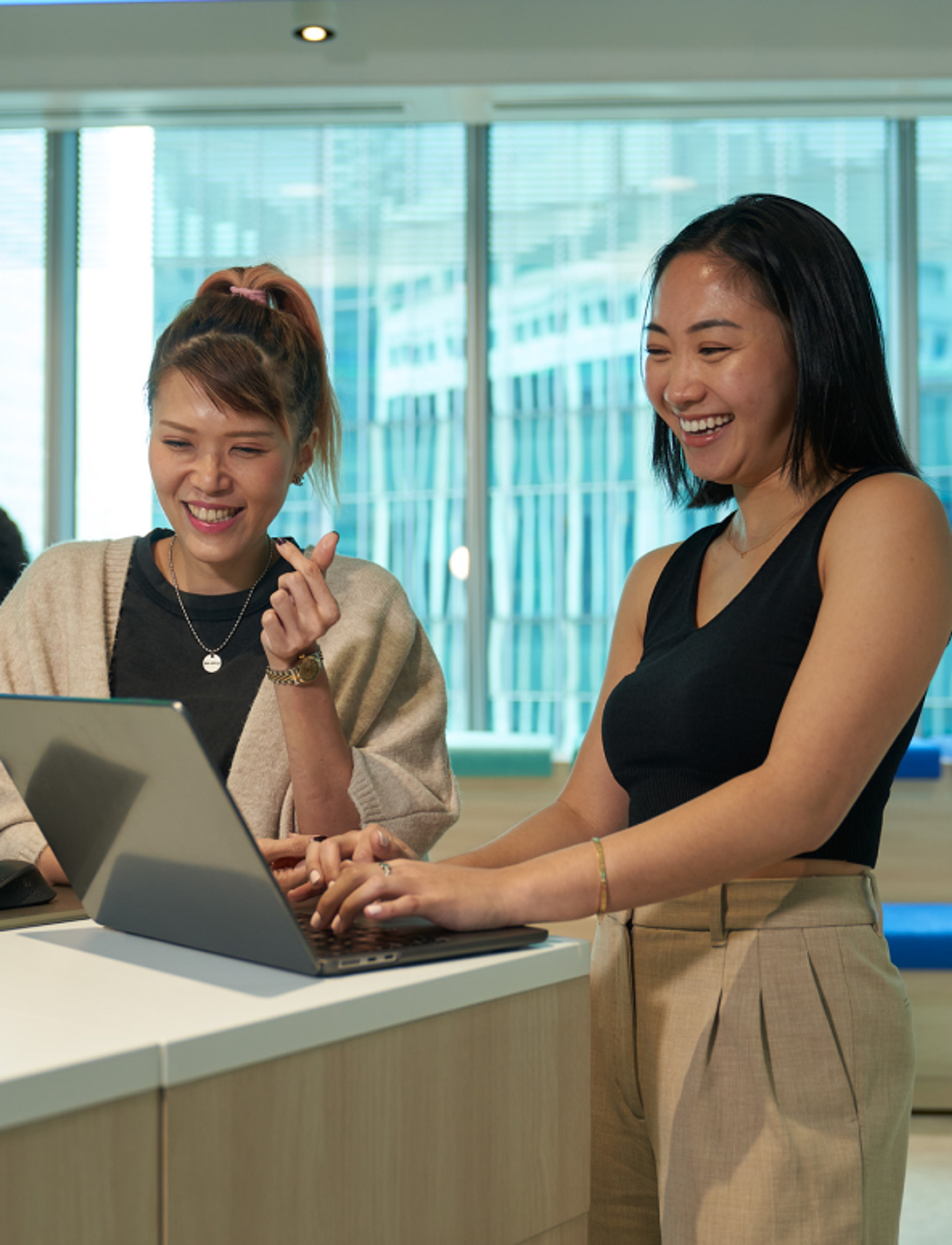 Two young female ByteDance employees smile as they work at their laptops.