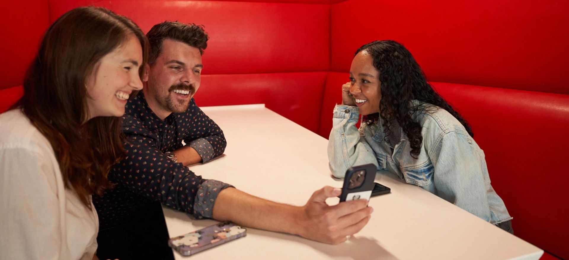 Three employees smile while looking at a phone.