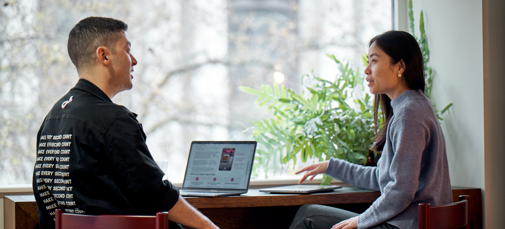 A male and a female TikTok employee sit and talk with an open laptop next to them.