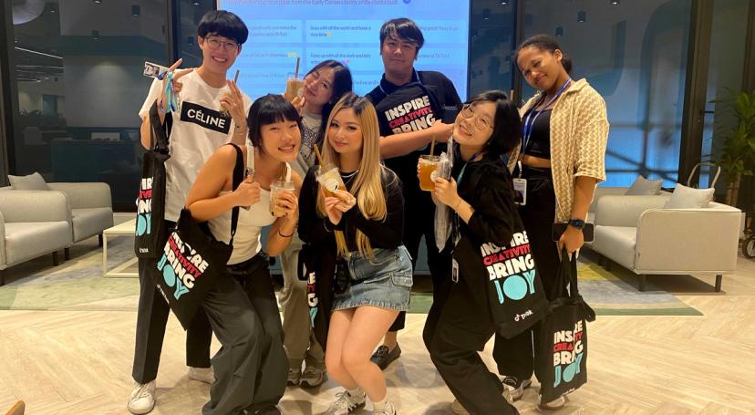 Seven participants in TikTok's Project Intern Program pose together holding boba beverages in an office setting.