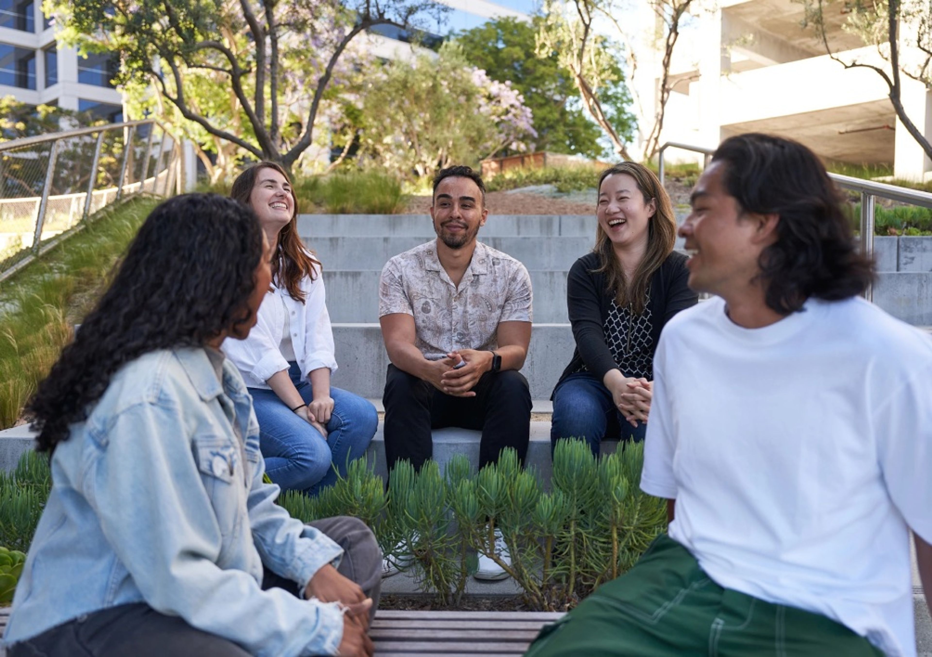 A diverse group of employees at a TikTok office in North America sit outside laughing and talking together.